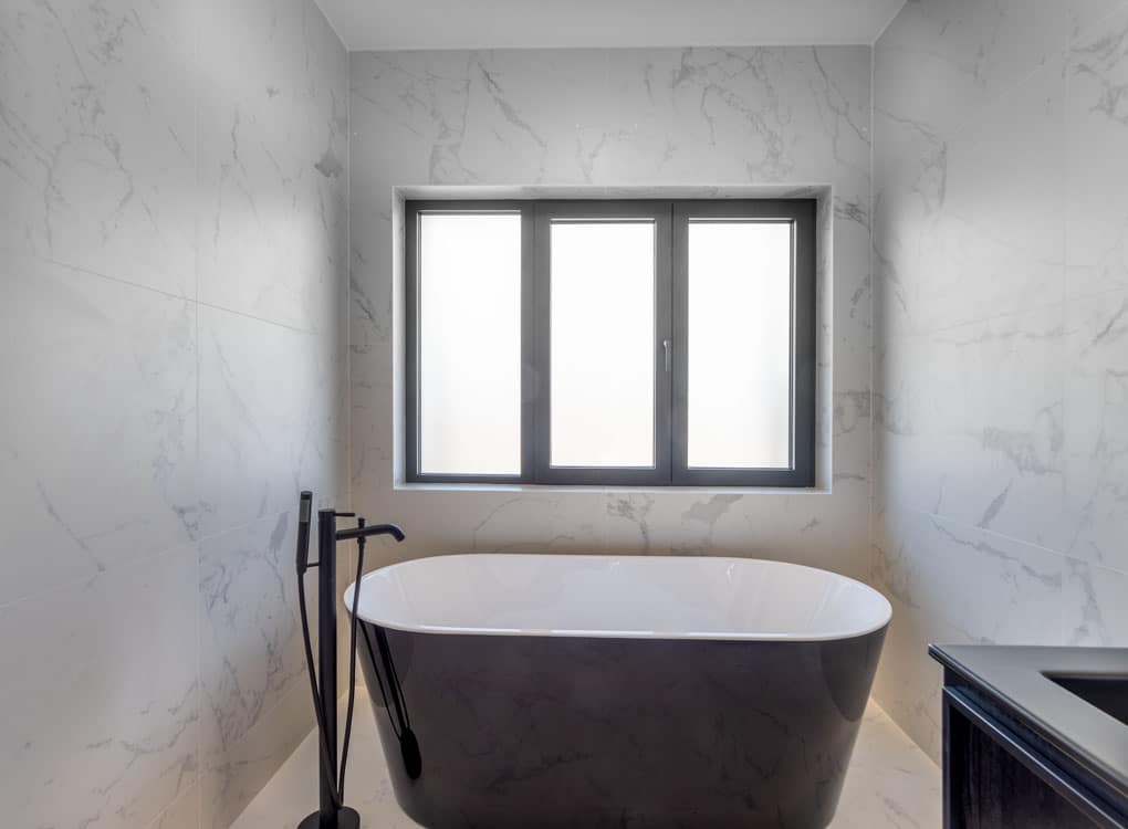 Salle de bain élégante avec baignoire noire, marbre clair et mobilier en bois sombre.