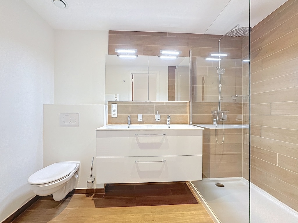 Salle de bain moderne, double vanité blanche, douche en verre, ambiance lumineuse et élégante.