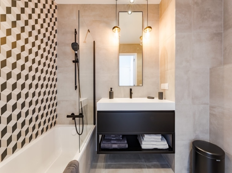 Salle de bain moderne avec mur graphique, baignoire élégante et éclairage chaleureux.