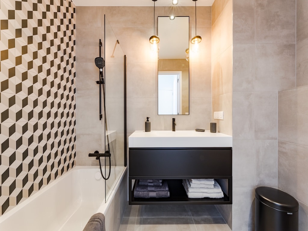 Salle de bain moderne avec mur graphique, baignoire élégante et éclairage chaleureux.