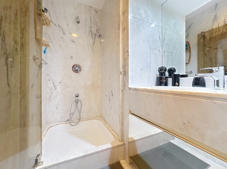 Salle de bain moderne avec douche en verre, marbre clair, grand miroir et design épuré.
