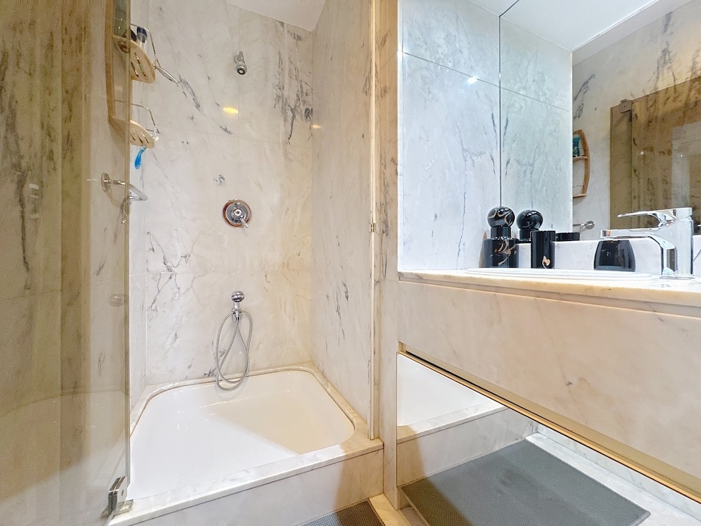 Salle de bain moderne avec douche en verre, marbre clair, grand miroir et design épuré.