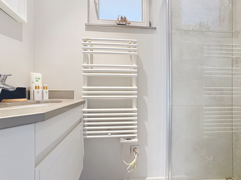 Salle de bain moderne avec mobilier blanc, douche en verre et radiateur à serviettes contemporain.