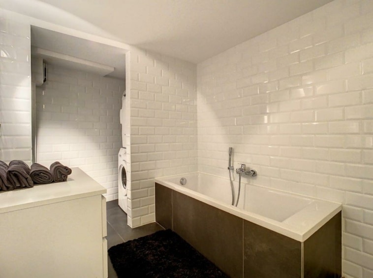 Salle de bain moderne avec douche, baignoire blanche, rangements épurés et espace laundry intégré.