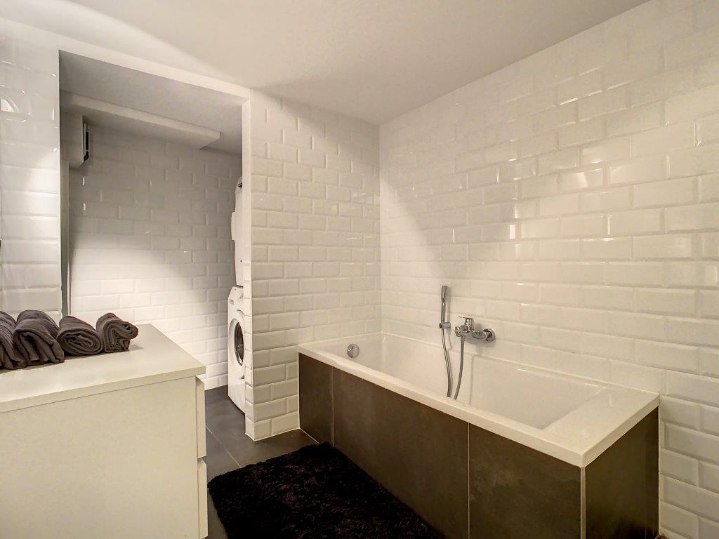 Salle de bain moderne avec douche, baignoire blanche, rangements épurés et espace laundry intégré.