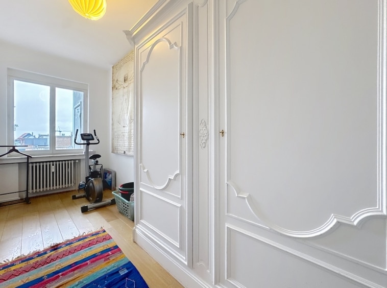 Salon lumineux et épuré avec mobilier élégant, tapis coloré, vélo d’appartement et lumière naturelle.