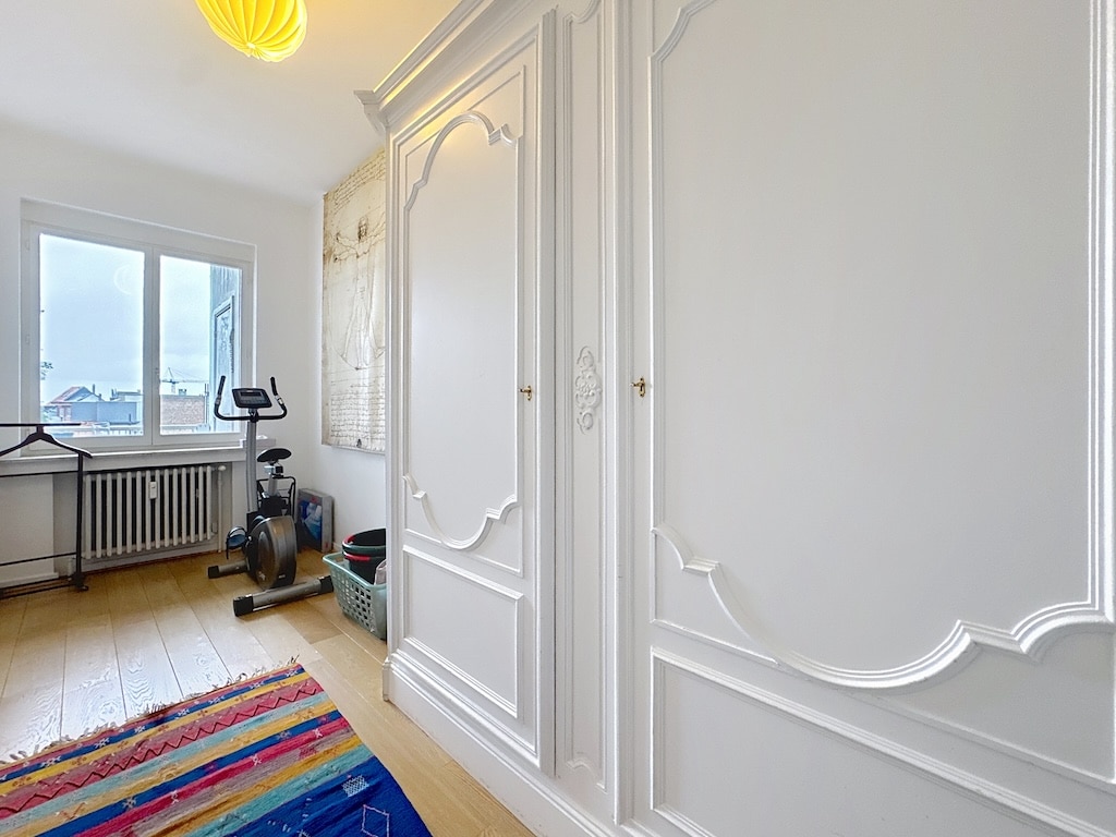 Salon lumineux et épuré avec mobilier élégant, tapis coloré, vélo d’appartement et lumière naturelle.
