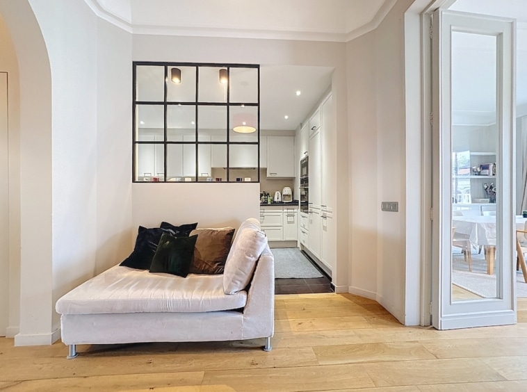 Salon contemporain avec canapé gris, verrière noire, cuisine blanche lumineuse et décoration minimalist