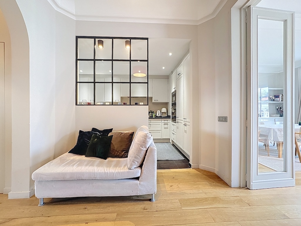 Salon contemporain avec canapé gris, verrière noire, cuisine blanche lumineuse et décoration minimalist