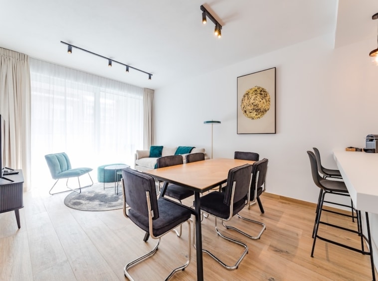Salon moderne lumineux avec espace repas, fauteuils teal et bar convivial, décor élégant et accueillant.