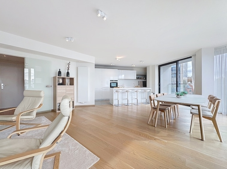 Salon moderne lumineux avec cuisine ouverte, mobilier épuré, grandes fenêtres et ambiance chaleureuse.