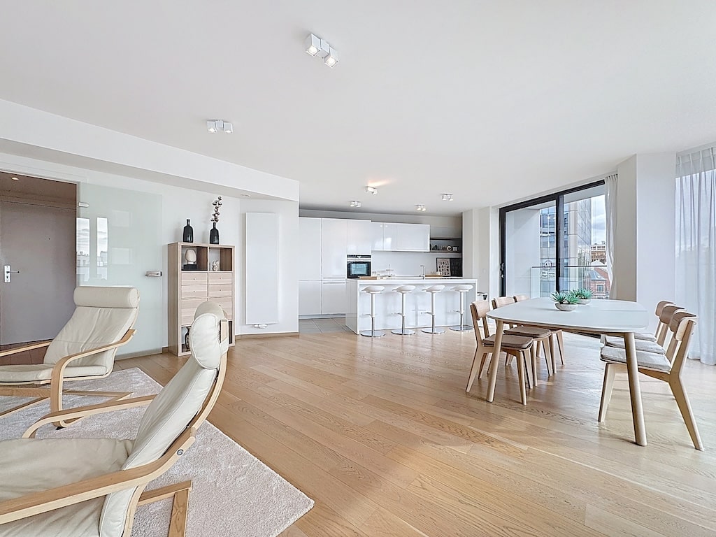 Salon moderne lumineux avec cuisine ouverte, mobilier épuré, grandes fenêtres et ambiance chaleureuse.