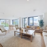 Salon moderne lumineux avec grandes fenêtres, mobilier en bois clair, vue extérieure et ambiance chaleureuse.