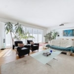 Salon lumineux avec canapé blanc, fauteuils noirs, plantes d’intérieur et espace repas moderne.