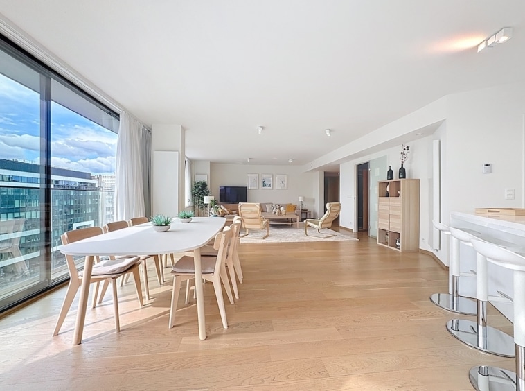 Salon moderne lumineux avec vue urbaine, mobilier en bois clair, espace détente et convivialité.