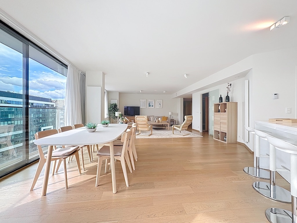 Salon moderne lumineux avec vue urbaine, mobilier en bois clair, espace détente et convivialité.