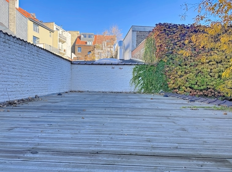Terrasse urbaine en bois avec végétation, vue sur ciel bleu et bâtiments modernes.