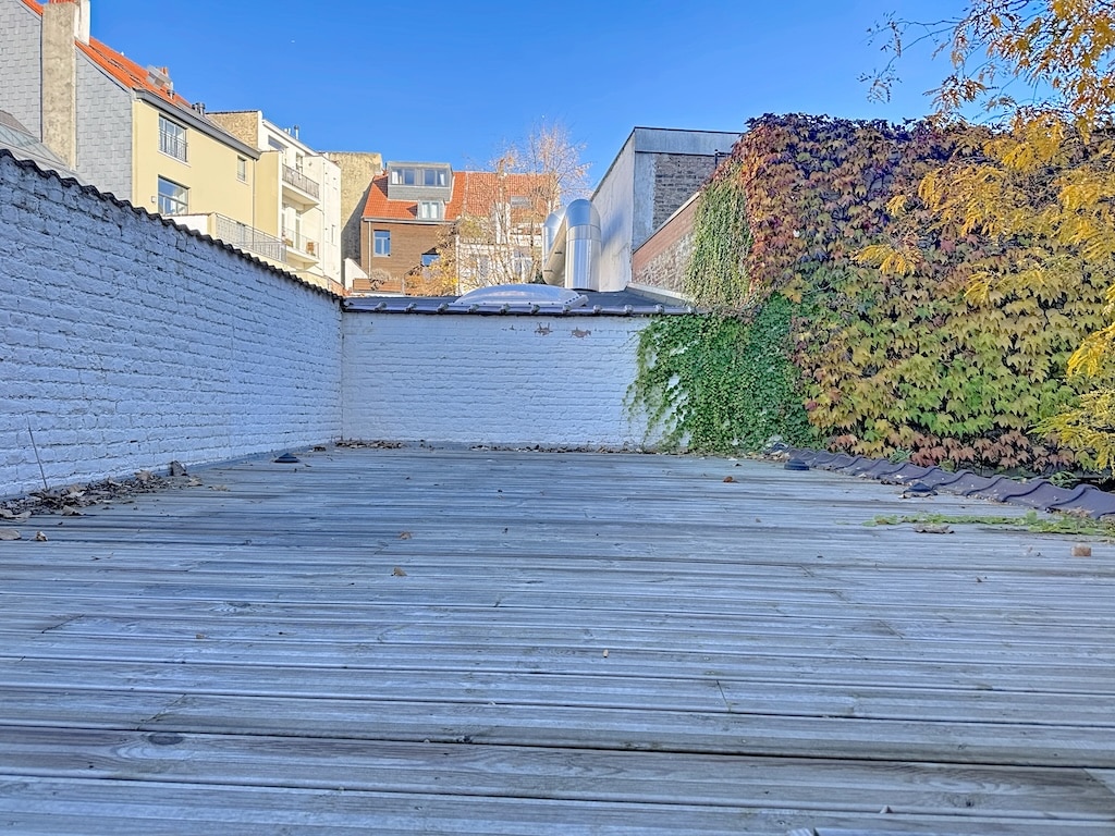 Terrasse urbaine en bois avec végétation, vue sur ciel bleu et bâtiments modernes.