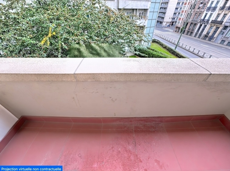 Balcon avec vue urbaine, arbre luxuriant et architecture moderne en arrière-plan.