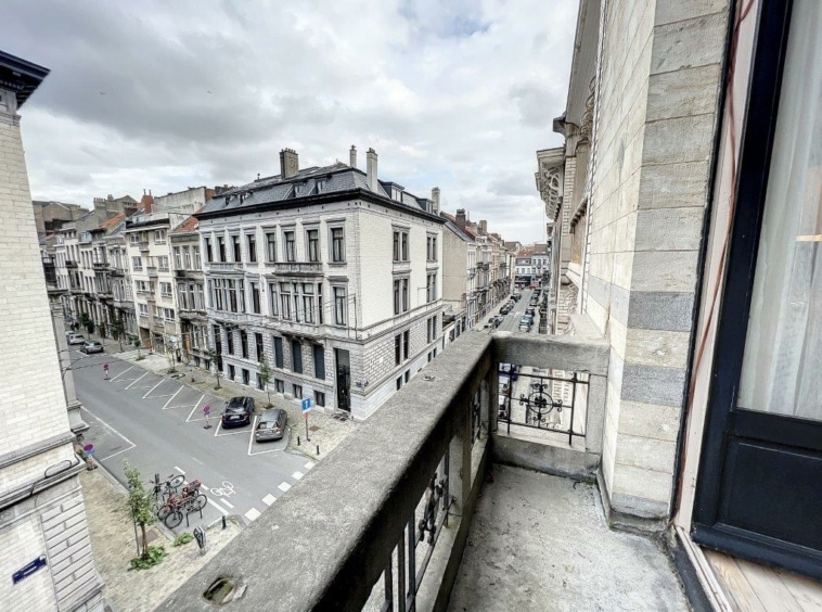 Balcon avec vue sur une rue historique européenne sous ciel gris, bâtiments ornés et ambiance urbaine.