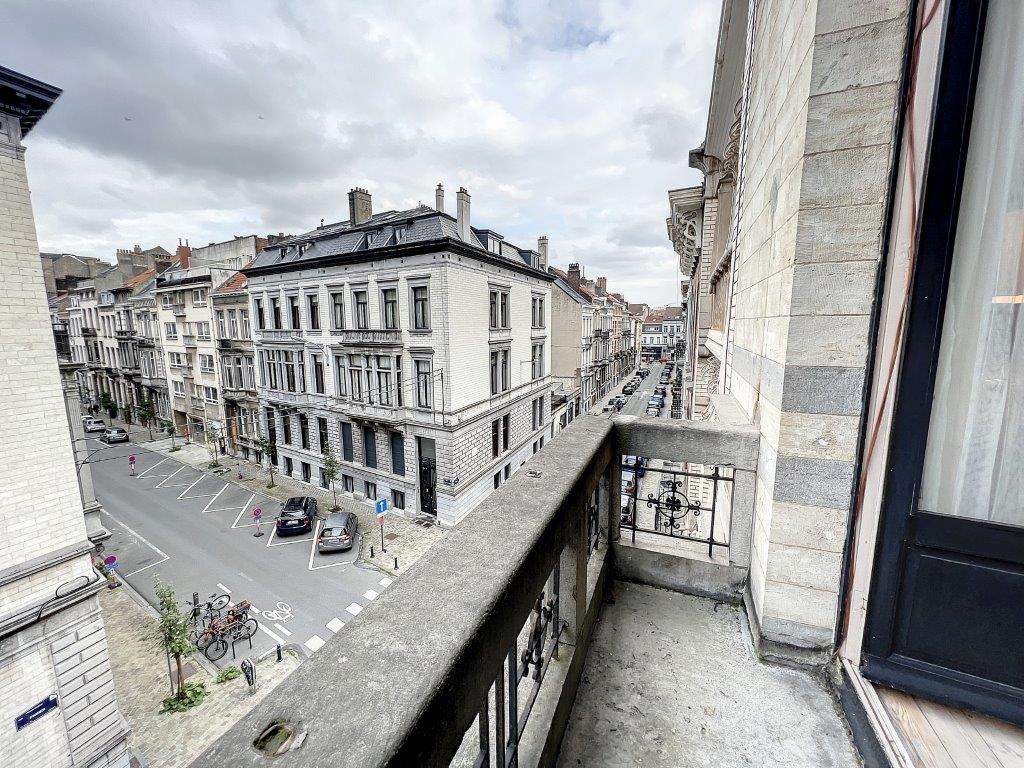 Balcon avec vue sur une rue historique européenne sous ciel gris, bâtiments ornés et ambiance urbaine.