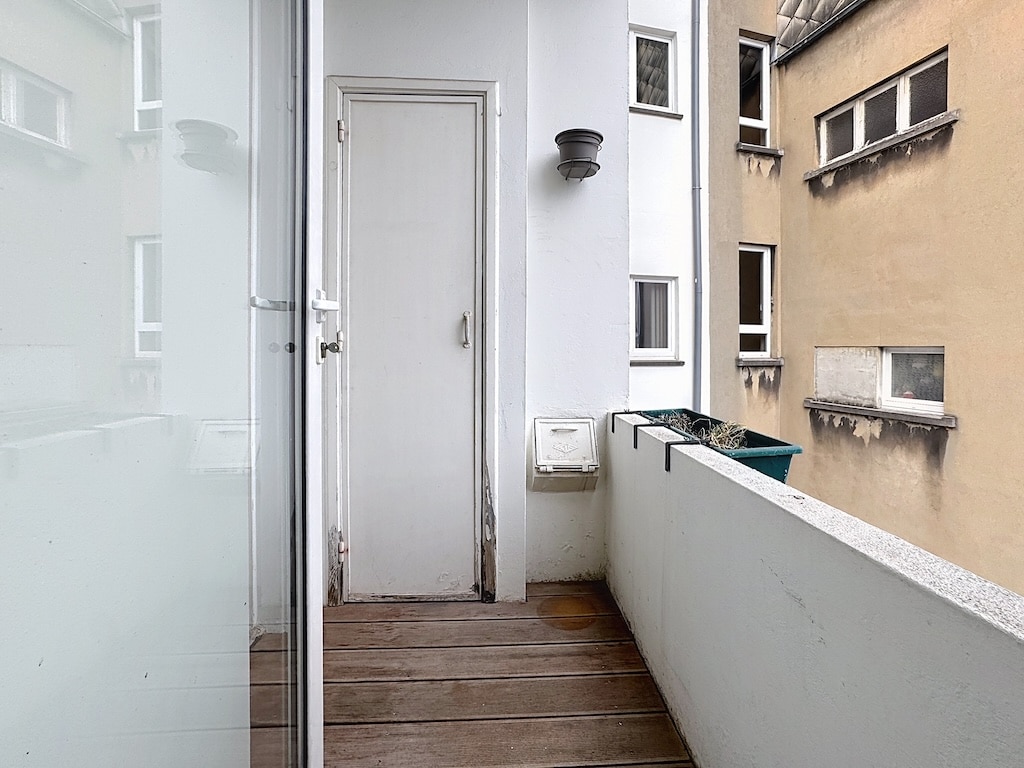 Balcon urbain moderne avec vue, sol en bois, jardinière vide et lumière discrète.