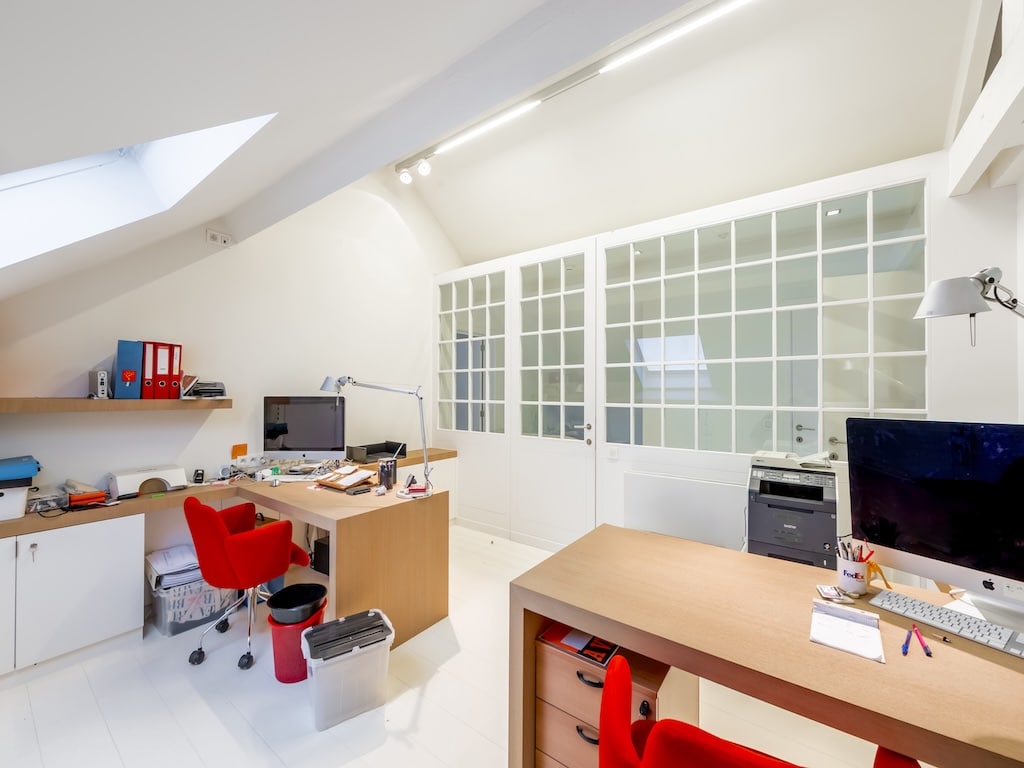 Bureau moderne lumineux avec deux espaces de travail, rangements rouges et porte en verre.