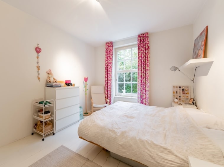 Chambre lumineuse avec lit crème, rideaux roses, mobilier blanc et ambiance chaleureuse.