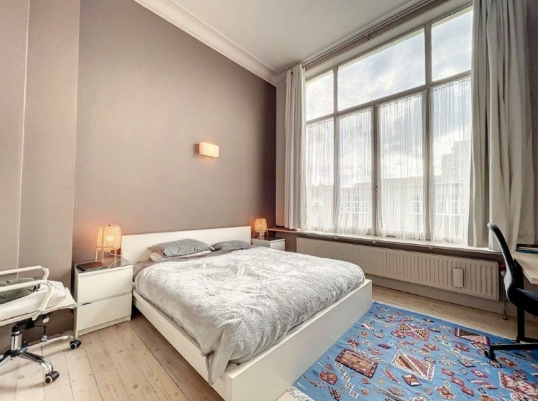 Chambre moderne lumineuse avec tapis coloré, lit gris, bureau noir et ambiance chaleureuse.