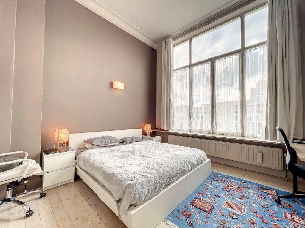 Chambre moderne lumineuse avec tapis coloré, lit gris, bureau noir et ambiance chaleureuse.