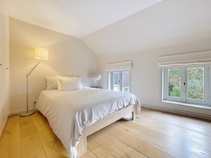 Chambre minimaliste lumineuse avec lit blanc mobilier en bois clair vue sur la verdure extérieure