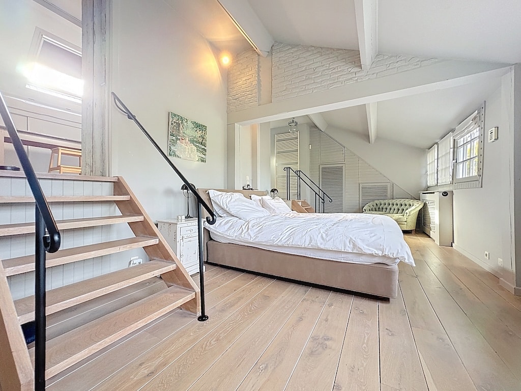 Lichte, minimalistische slaapkamer met trap, groene fauteuil, hout en natuurlijk licht.