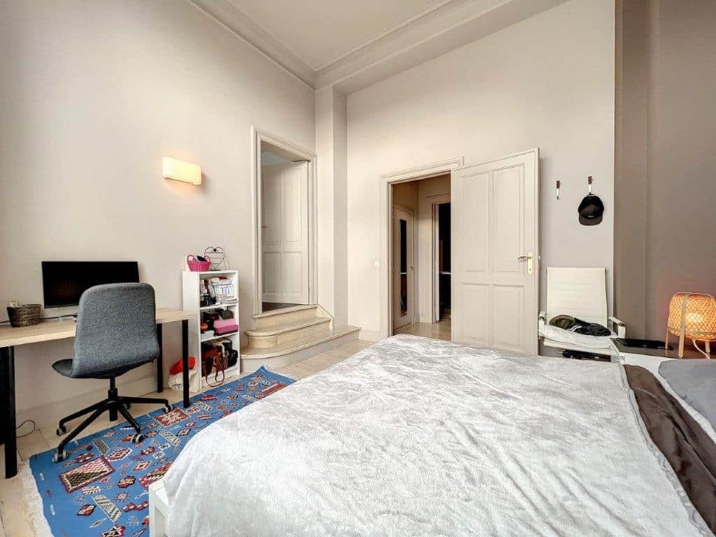 Chambre lumineuse moderne avec lit blanc, espace de travail organisé et ambiance chaleureuse.