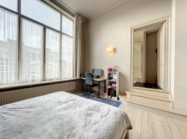 Chambre lumineuse avec espace de travail moderne, grand lit, murs neutres, ambiance paisible et chaleureuse.
