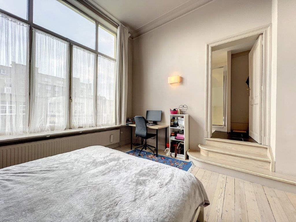 Chambre lumineuse avec espace de travail moderne, grand lit, murs neutres, ambiance paisible et chaleureuse.