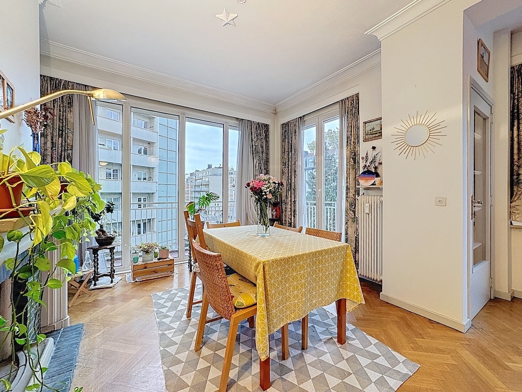 Coin repas cosy avec vue urbaine, plantes vertes, décoration chaleureuse et lumineux.