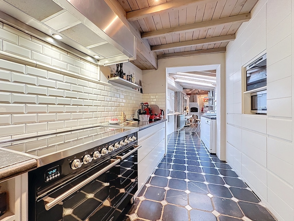 Moderne keuken met roestvrijstalen kookplaat, houten balken, zwarte vloer en lichte inrichting.