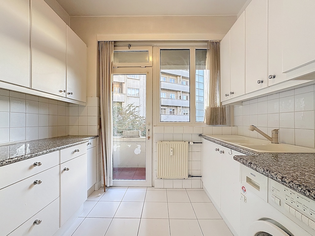 Cuisine moderne lumineuse avec plans en granite, fenêtre avec balcon, design pratique et épuré.