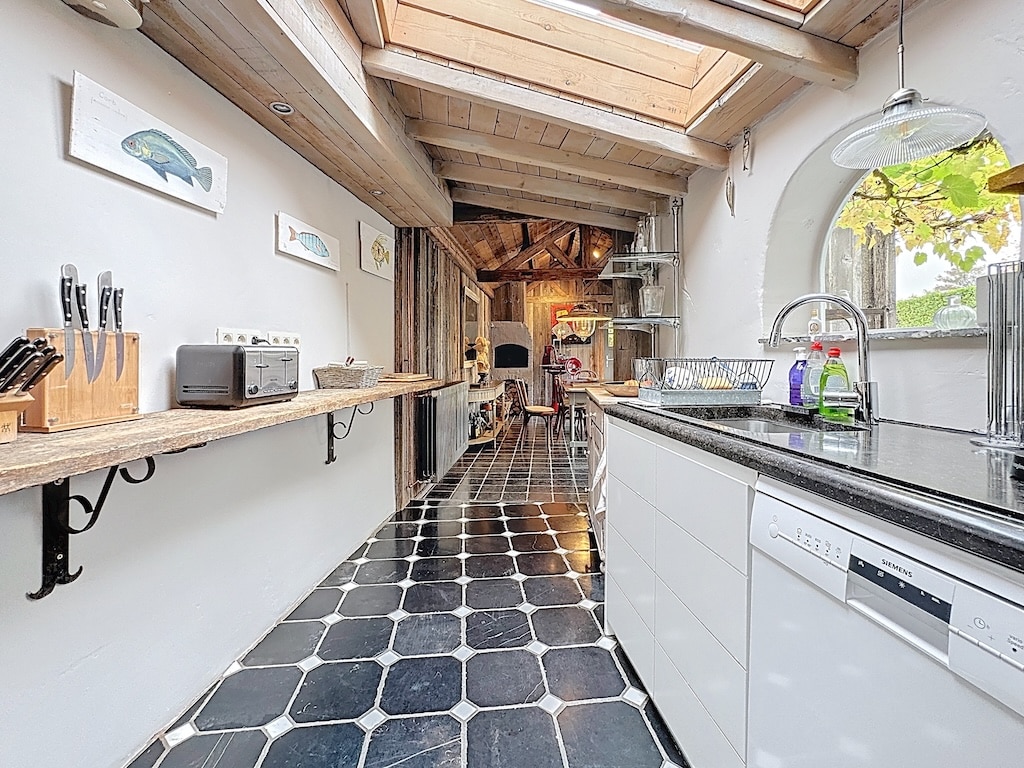 Lichte, moderne, rustieke keuken met houten plafond, zwarte tegelvloer en maritieme inrichting.