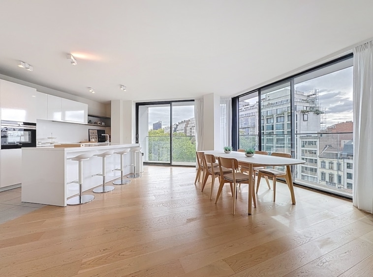 Cuisine moderne lumineuse avec îlot, table en bois, grandes fenêtres et vue panoramique sur la ville.