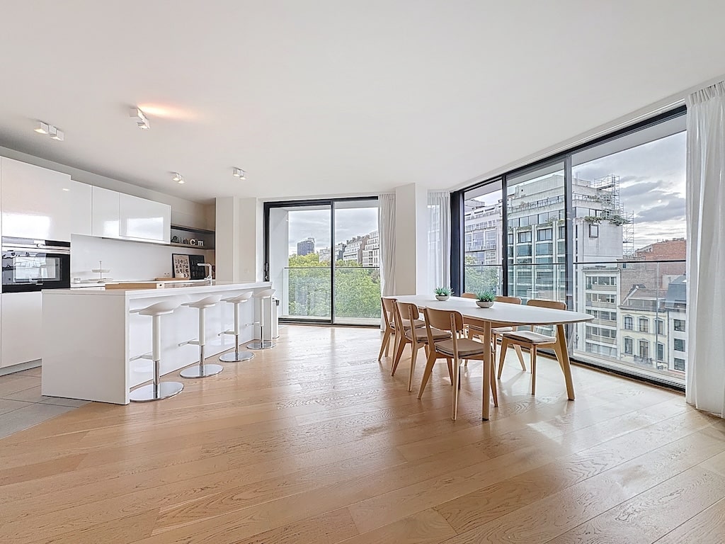 Cuisine moderne lumineuse avec îlot, table en bois, grandes fenêtres et vue panoramique sur la ville.