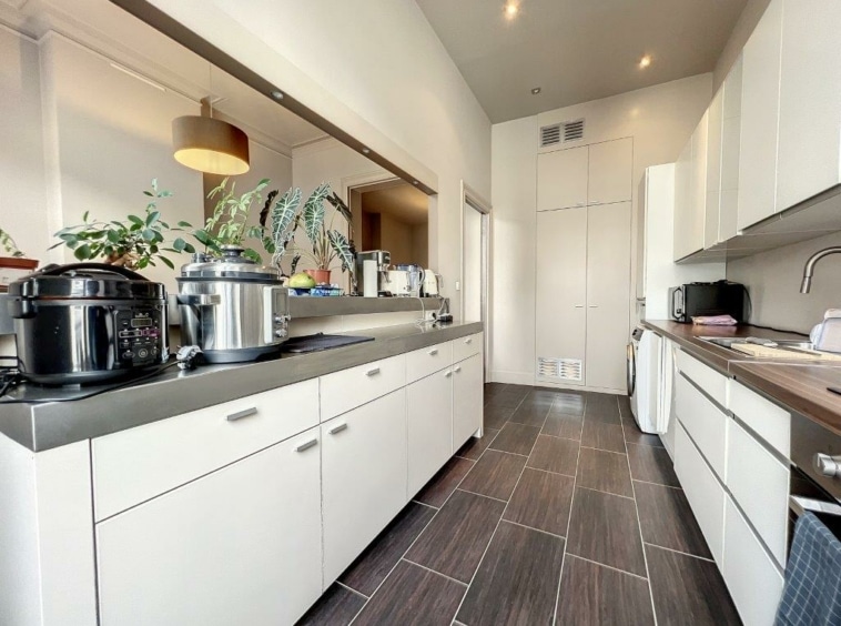 Cuisine moderne minimaliste avec éclairage chaud, armoires blanches, plans foncés et plantes décoratives.