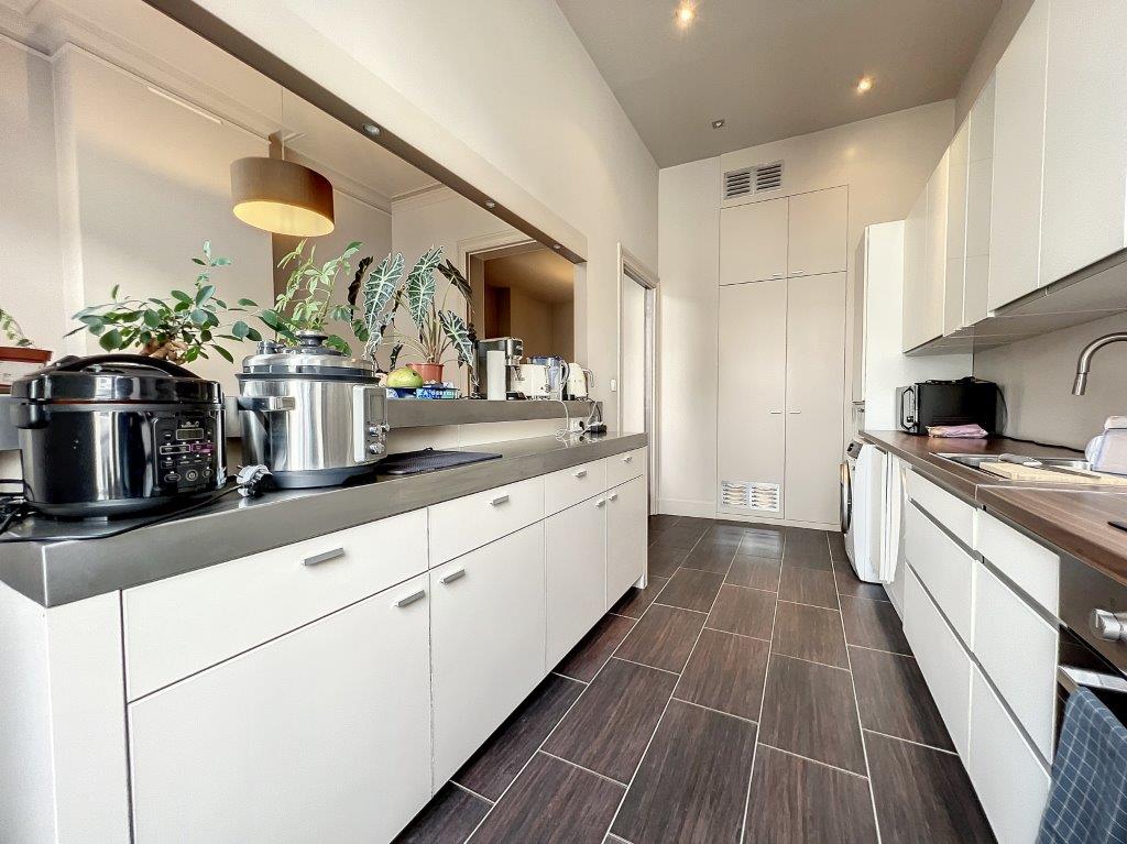 Cuisine moderne minimaliste avec éclairage chaud, armoires blanches, plans foncés et plantes décoratives.