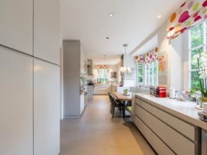 Cuisine moderne minimaliste avec îlot central, meubles neutres, fenêtres colorées et éclairage convivial.