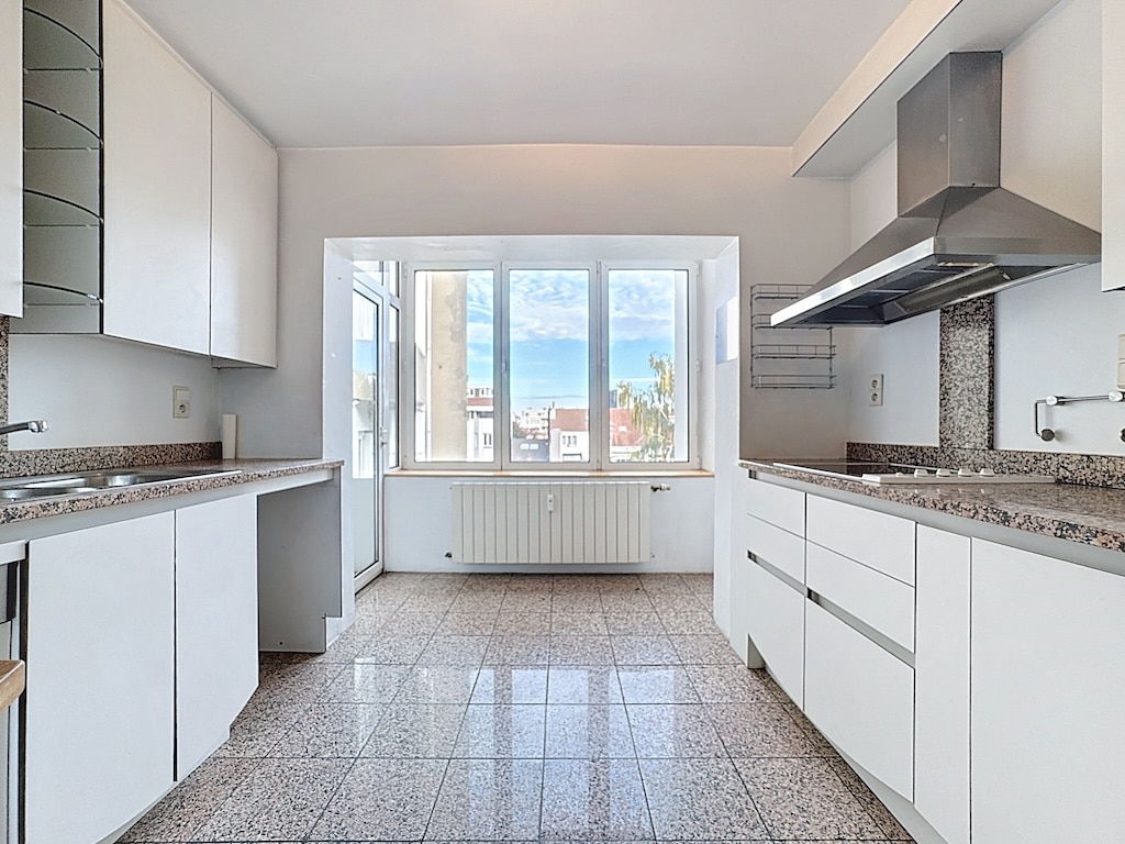 Cuisine moderne minimaliste avec plans en granit, armoires blanches, studio lumineux et électroménagers intégrés.