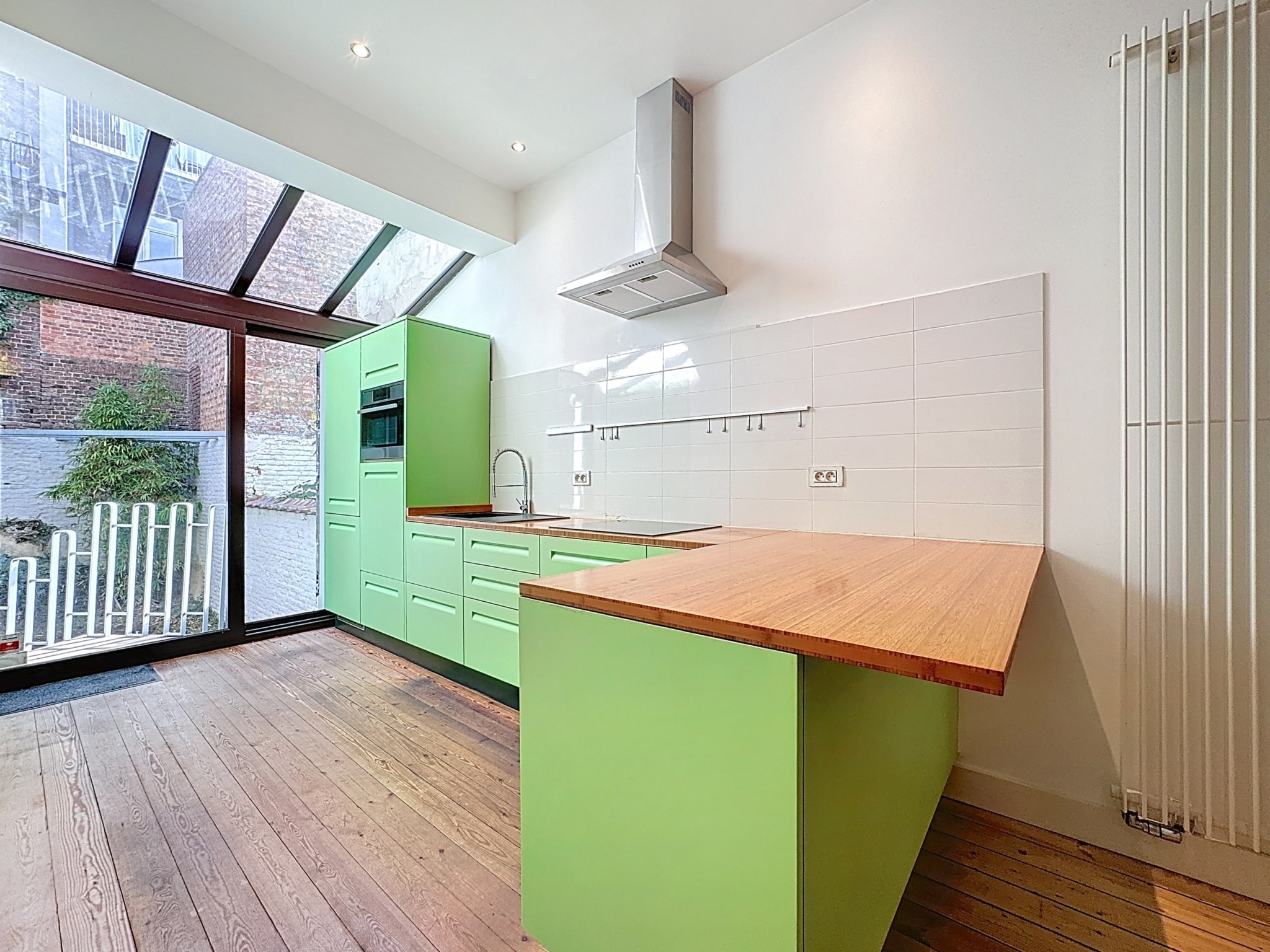 Cuisine moderne verte avec plan en bois, grande baie vitrée, intérieur lumineux et chaleureux.