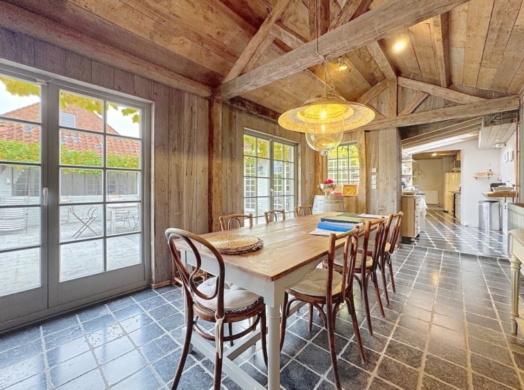 Lichte, rustieke eetkamer met houten tafel, vintage stoelen en weelderig uitzicht op de buitenlucht.