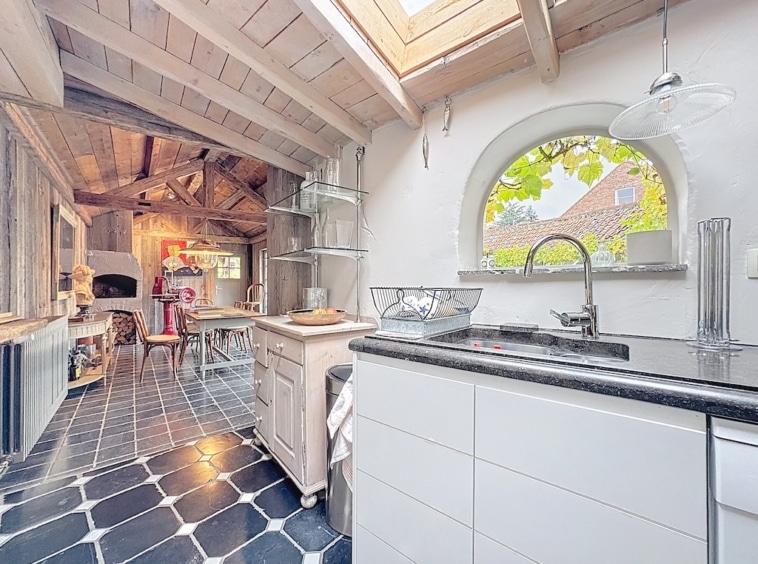Moderne, rustieke keuken met uitzicht op de natuur, zwart eiland, houten balken en natuurlijk licht.