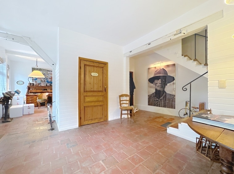 Lichte hal met kunstwand, moderne trap en warme terracotta vloer.