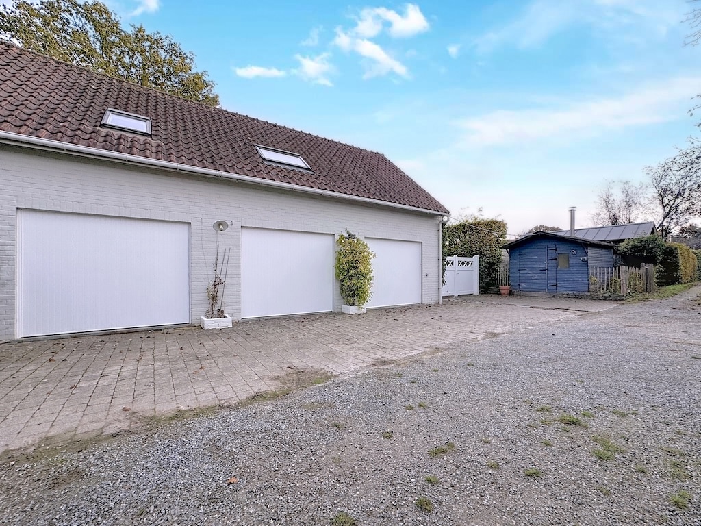 Moderne witte garage met schuin dak, parkeerplaats op grind, rustige omgeving en bomen op de achtergrond
